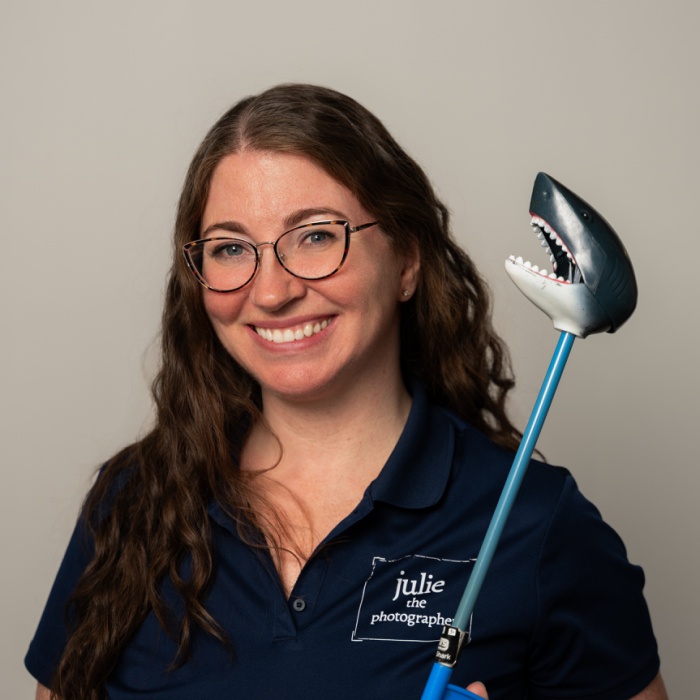 headshot of Julie wearing a navy polo and holding a toy shark